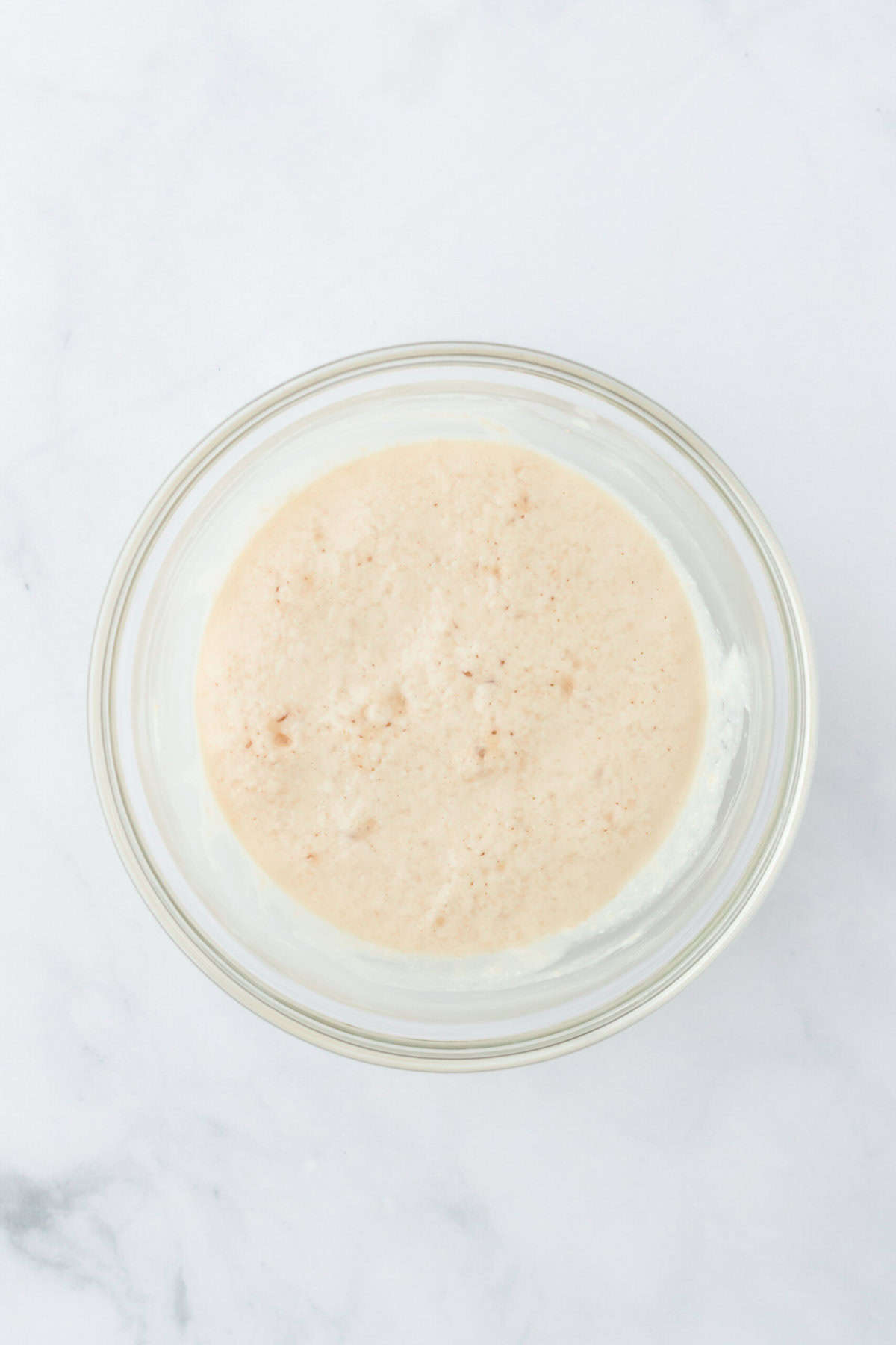 Foamy warm yeast mixture in clear bowl on white countertop