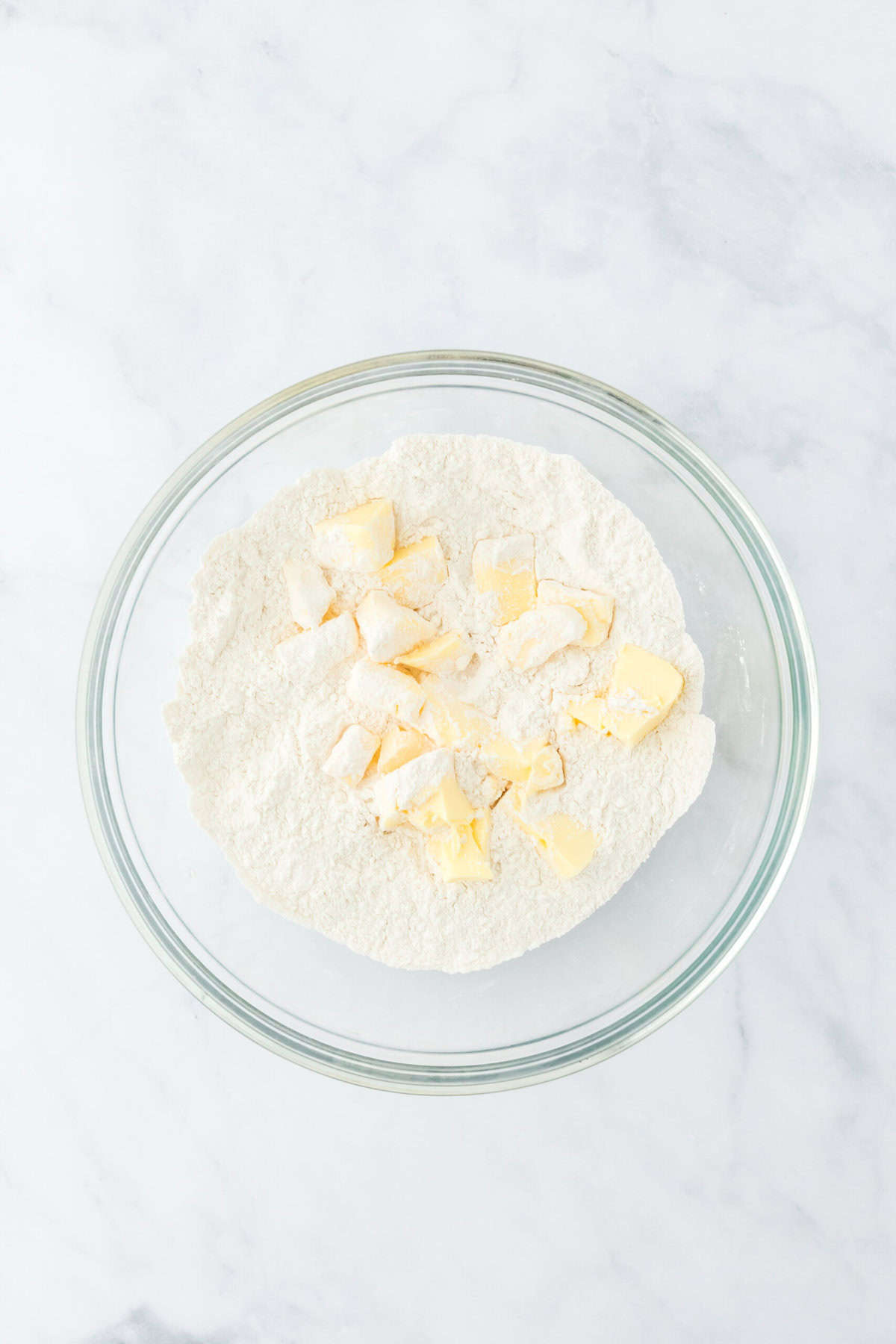 Butter flavored shortening cubes in flour mixture to make biscuits in a large bowl on white countertop