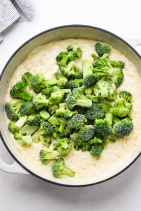 Frozen broccoli florets being added to a cheesy cream sauce after thickening