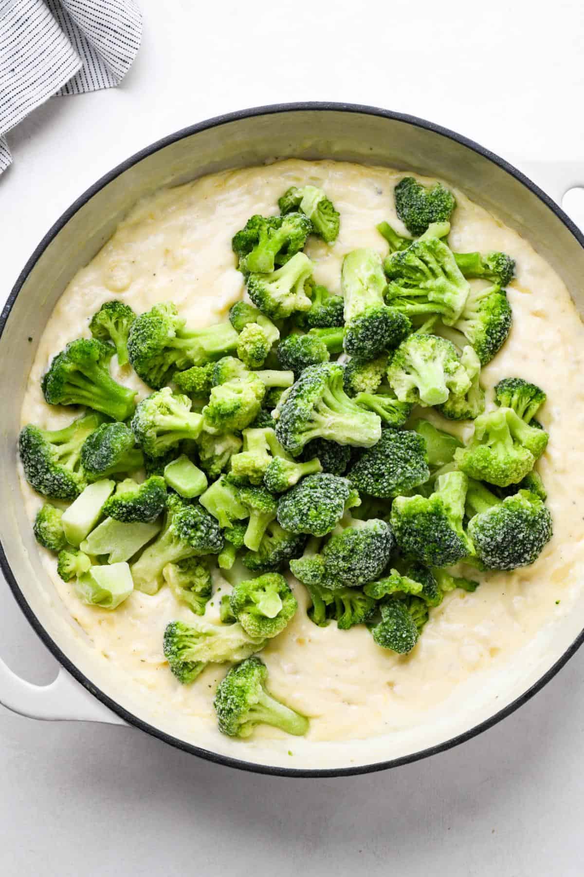 Frozen broccoli florets added on top of the creamy mixture in a white pot