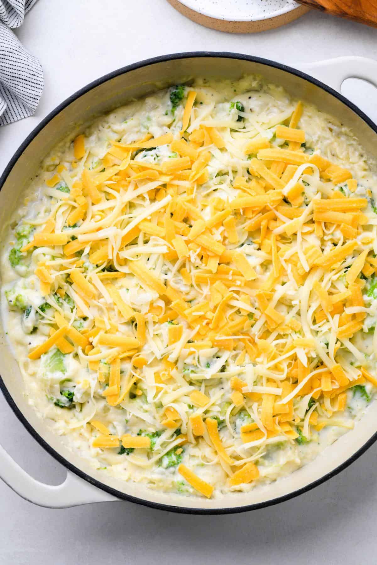 The creamy broccoli mixture topped with shredded cheddar and Swiss cheese in the pot
