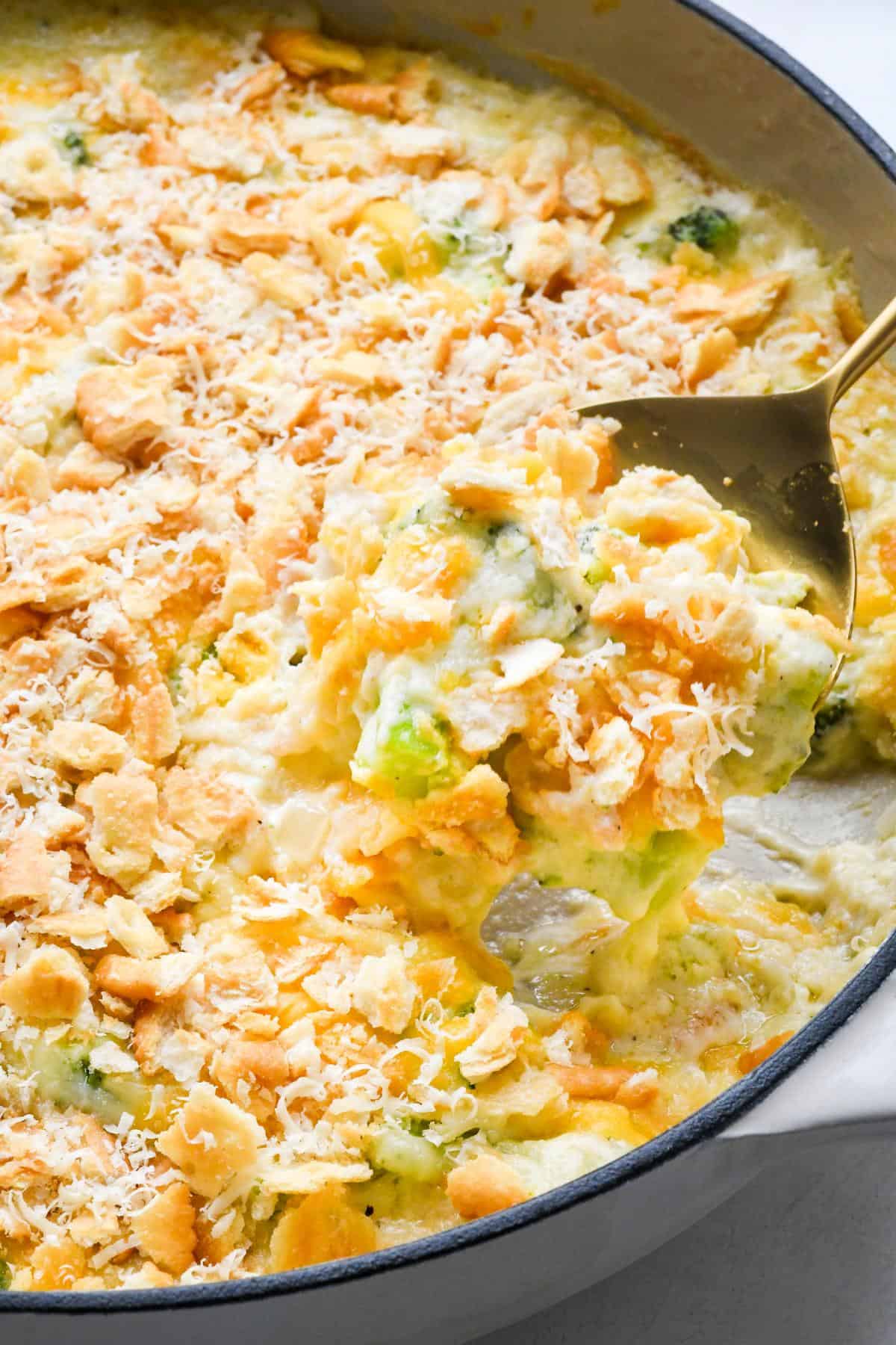 Closeup of a golden cheesy broccoli casserole being scooped out with a gold serving spoon