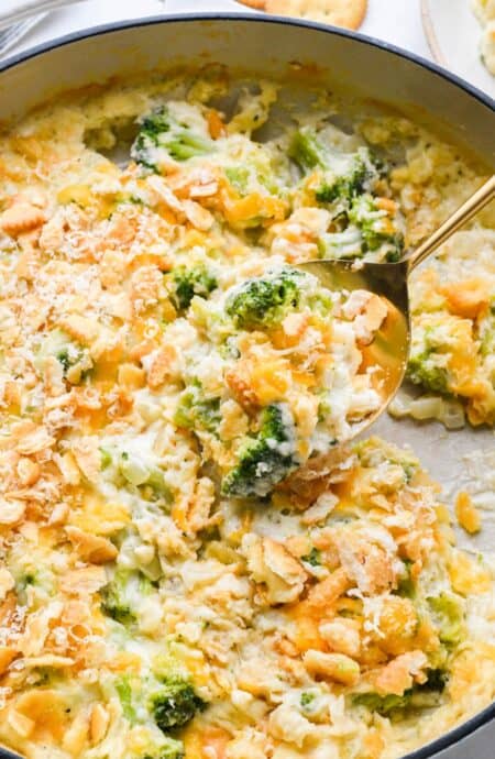 A spoonful of broccoli cheese casserole being lifted, showing a gooey texture with broccoli and cracker topping