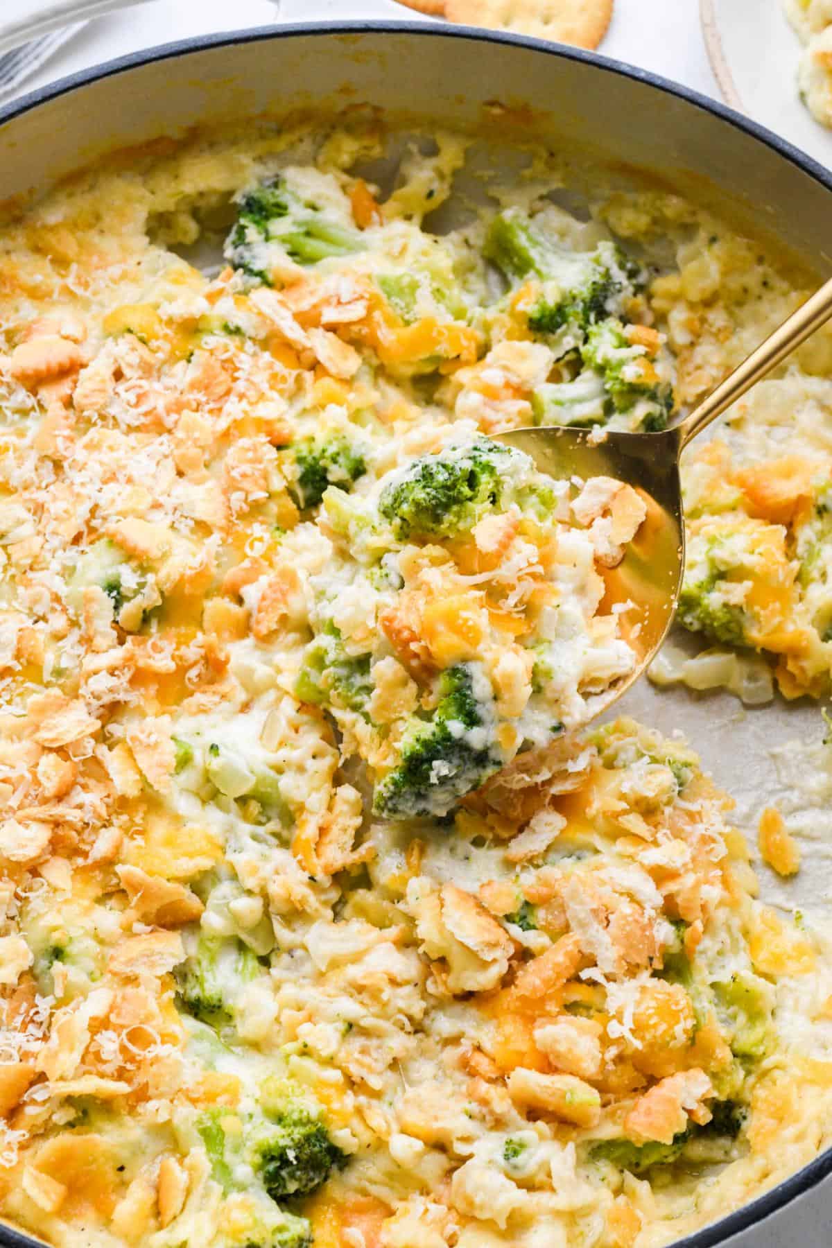A spoonful of broccoli cheese casserole being lifted, showing a gooey texture with broccoli and cracker topping