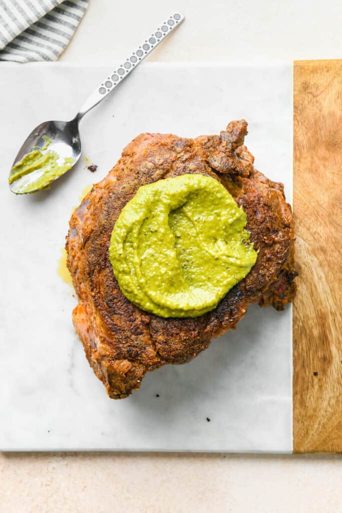 Pesto being spread on a chuck roast on white countertop