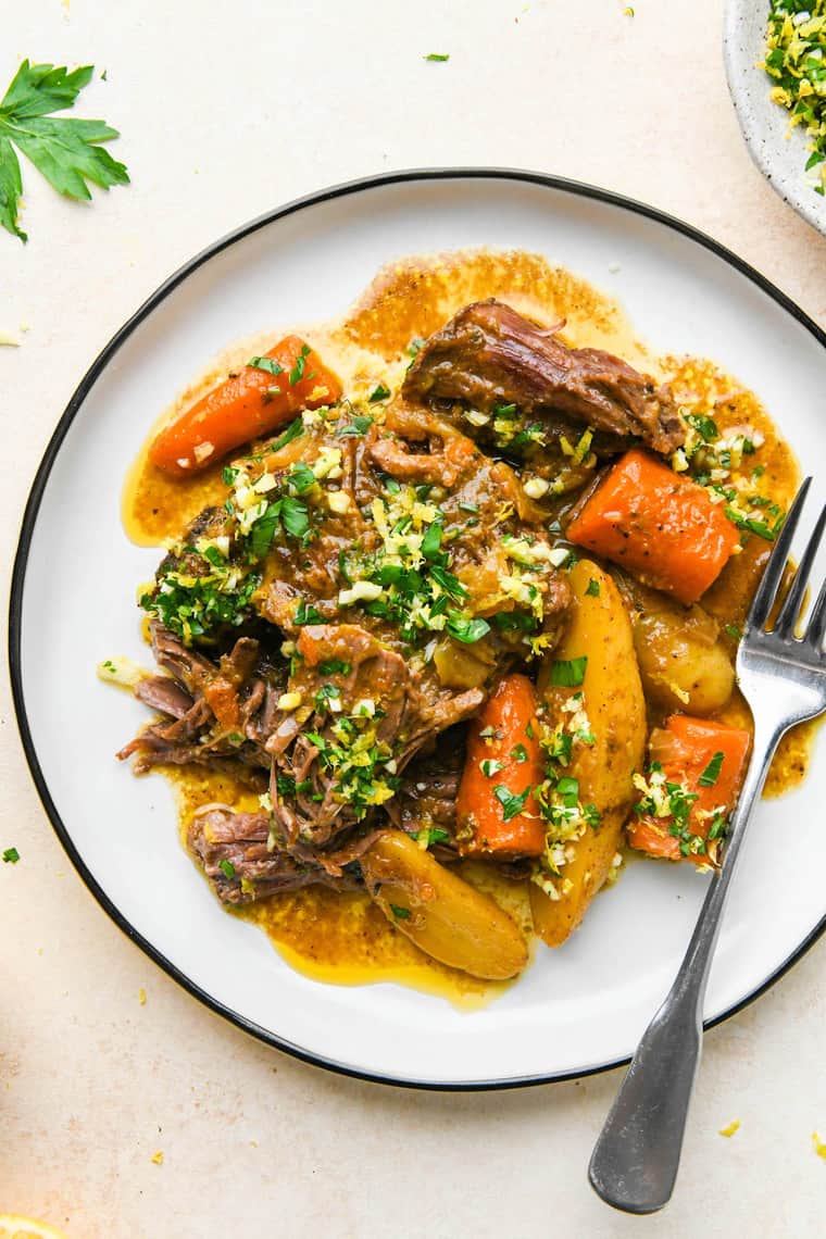 A large dish of pot roast ready to enjoy on a white dish with a silver fork
