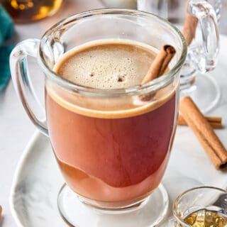 A close up of a glass of hot buttered rum with a cinnamon stick against a white background