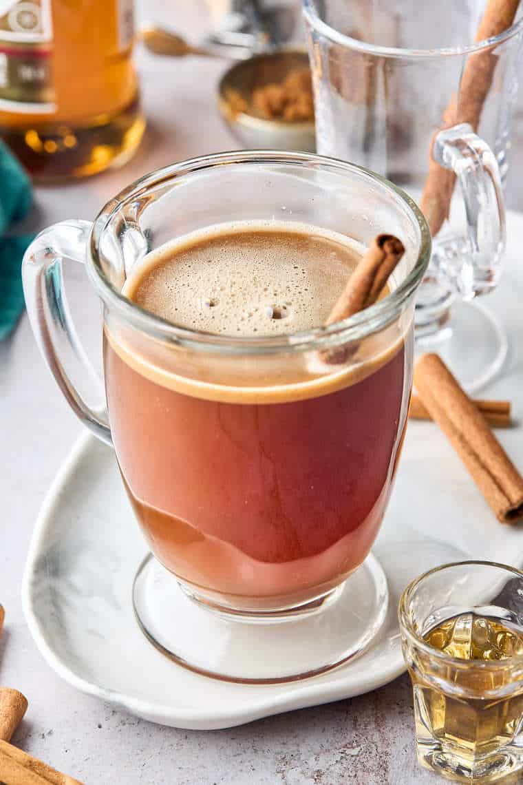 A close up of a glass of hot buttered rum with a cinnamon stick against a white background