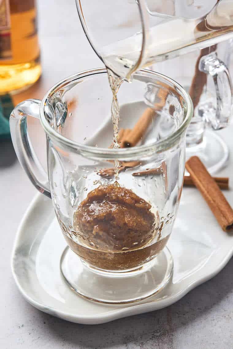 A splash of rum being poured in a glass over butter mixture to make a cocktail