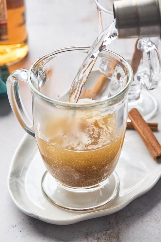 Hot water being poured over rum and butter mixture in a clear glass mug