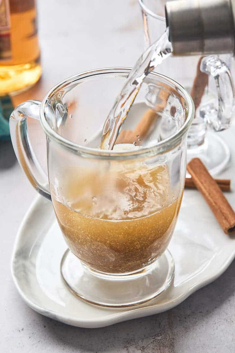 Hot water being poured over rum and butter mixture in a clear glass mug