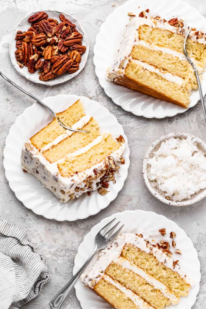 Three slices of yellow cake with cream cheese frosting and pecans on white plates
