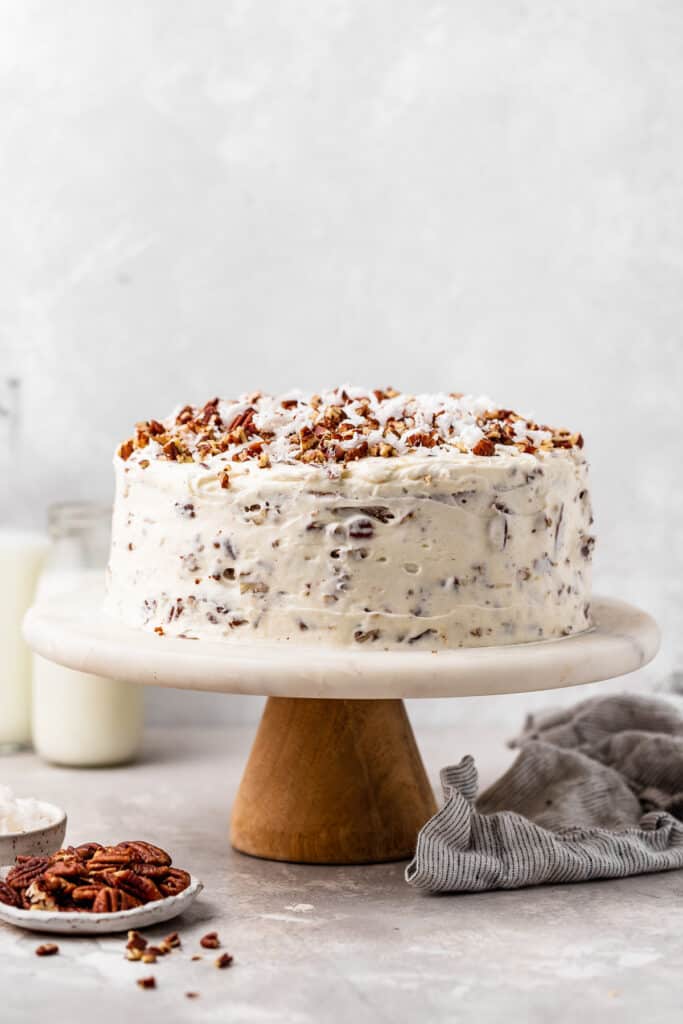 An Italian Crean Cake on a white and wooden cake stand against a gray background ready to serve