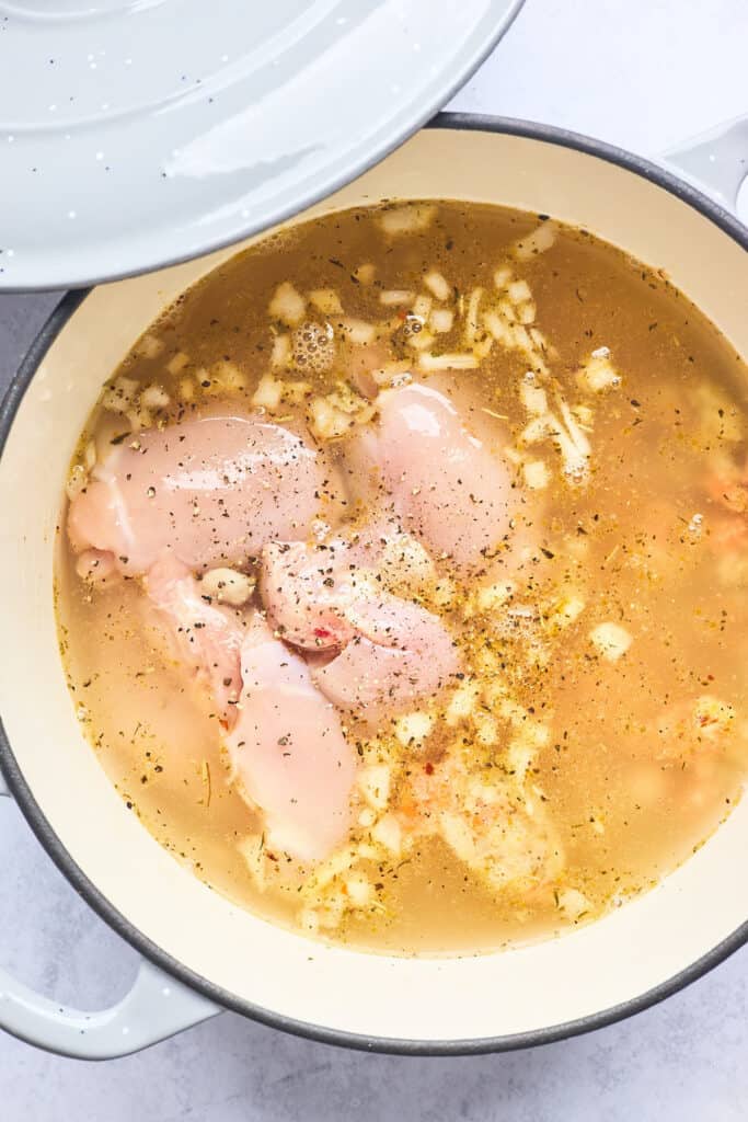Chicken thighs and chicken broth going into a large dutch oven