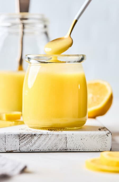 A close up of a jar of homemade lemon curd with a spoon scooping some out