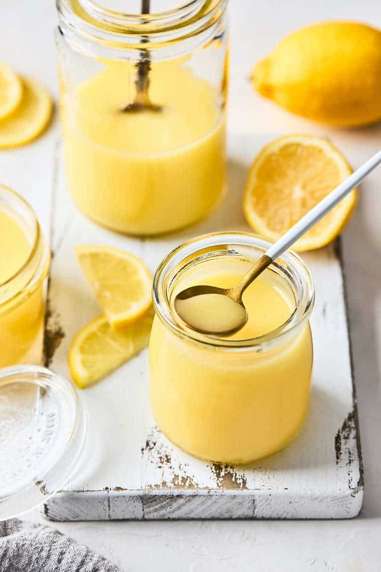 Two jars of homemade lemon curd with a small spoon lifting some