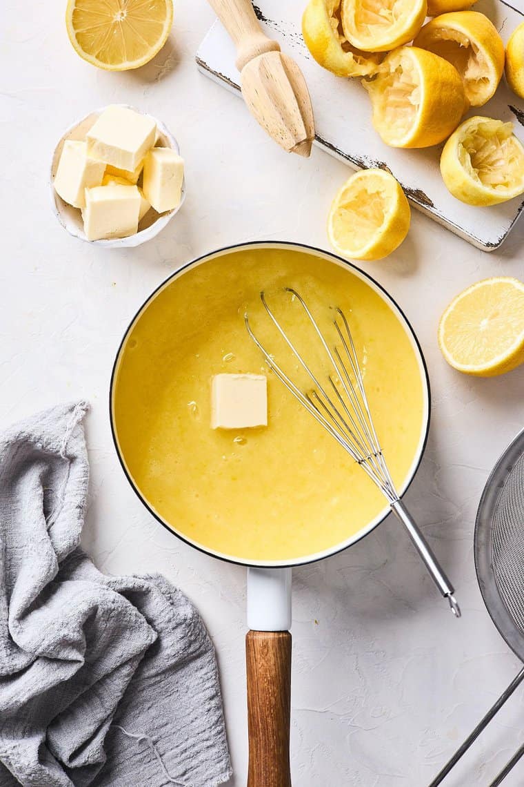 Lemon curd being cooked in a pot with butter being whisked in