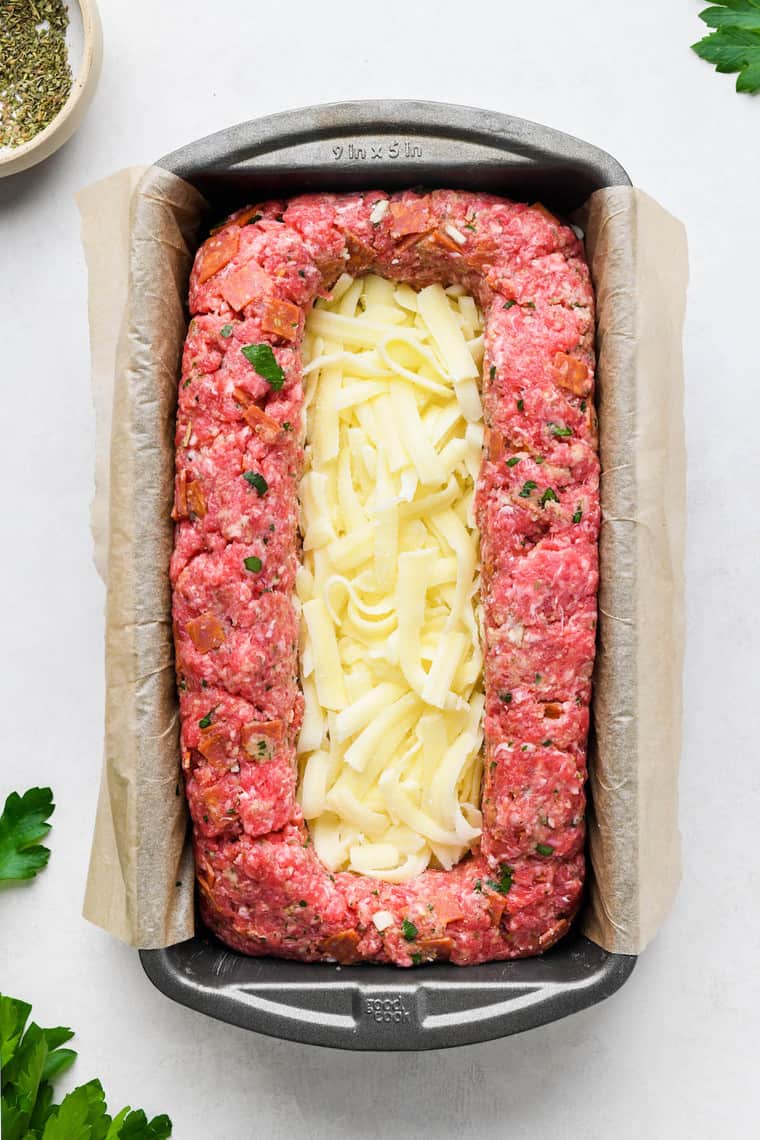 A meatloaf in a pan ready to bake with shredded cheese in the center