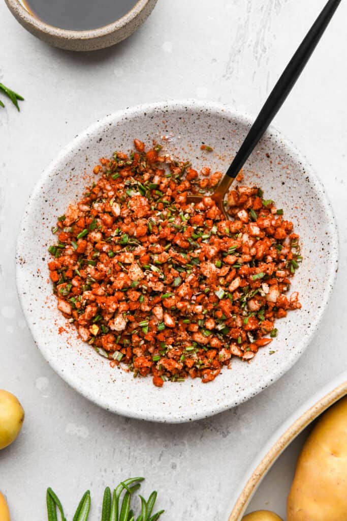 Several seasonings and aromatics in a white bowl before mixing together