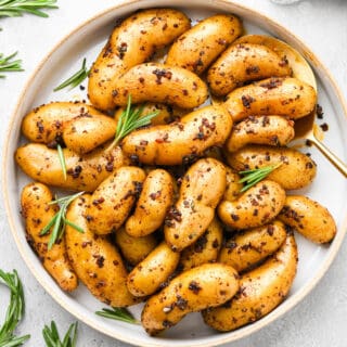 Roasted fingerling potatoes topped with herbs on a white plate ready to serve