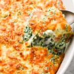 Baked cheesy spinach gratin with a spoon lifting some out of a casserole dish