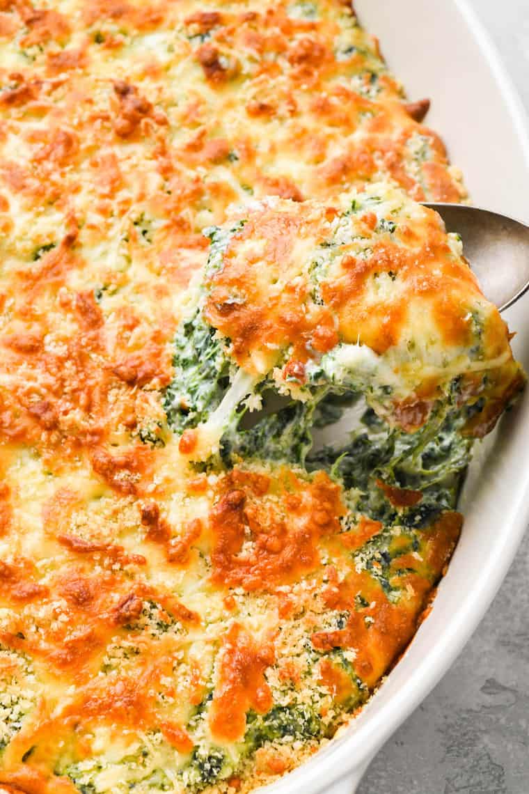 Baked cheesy spinach gratin with a spoon lifting some out of a casserole dish