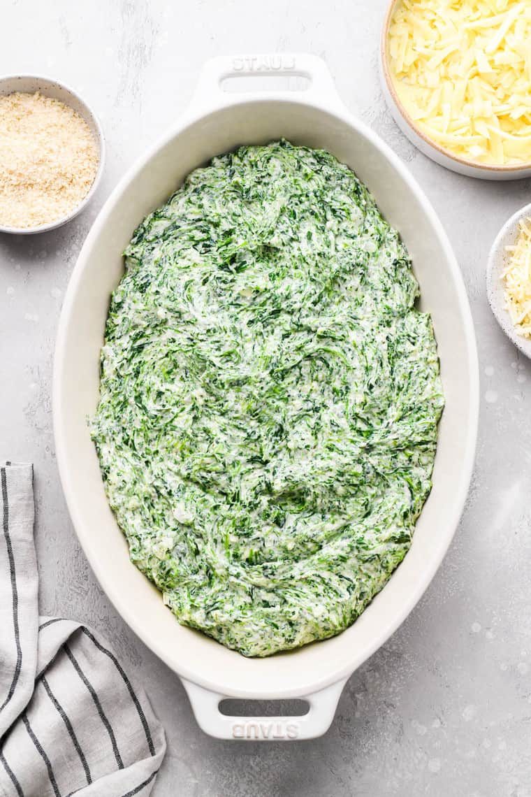 Creamy spinach in a white casserole dish with shredded cheeses surrounding it