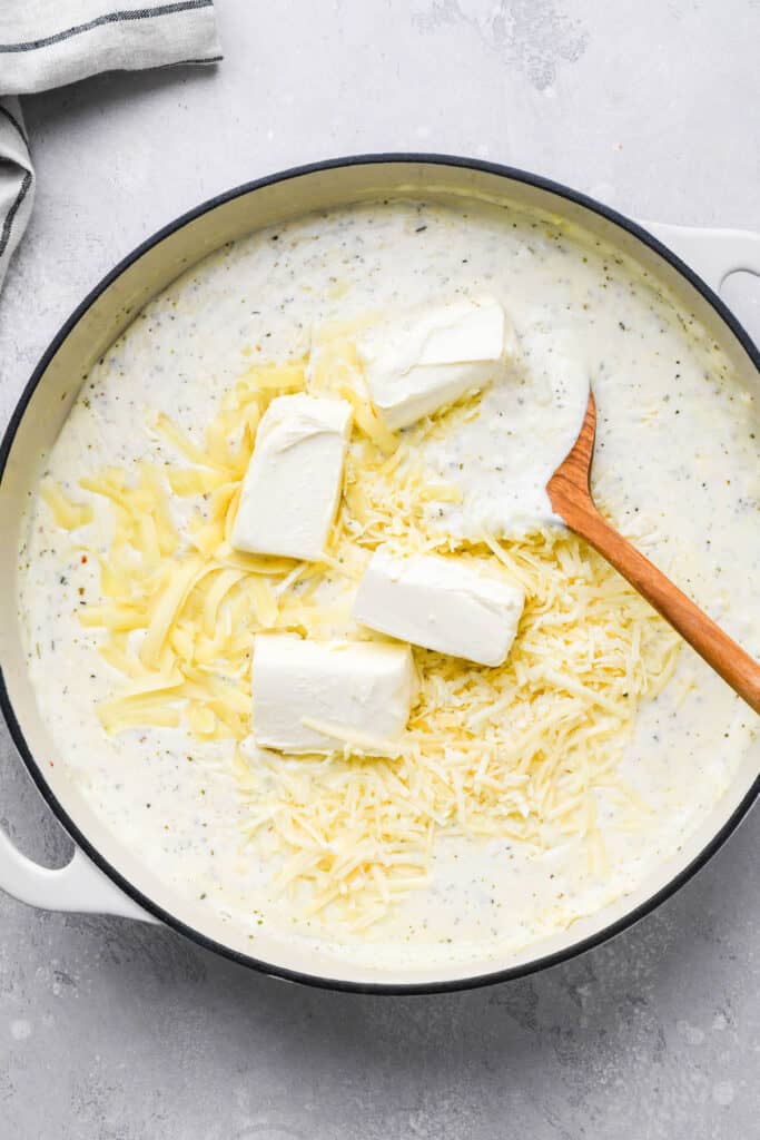 Cream cheese and shredded cheeses being whisked into a cream sauce