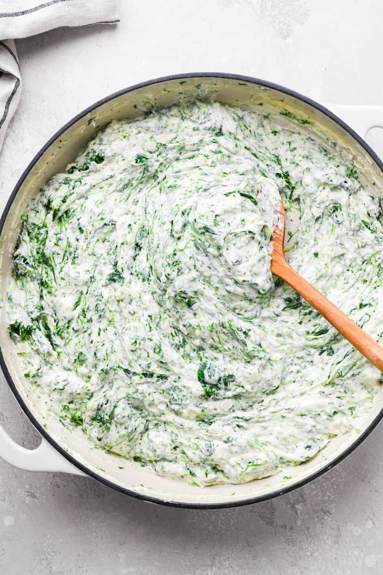 Creamed spinach being stirred with a wooden spoon