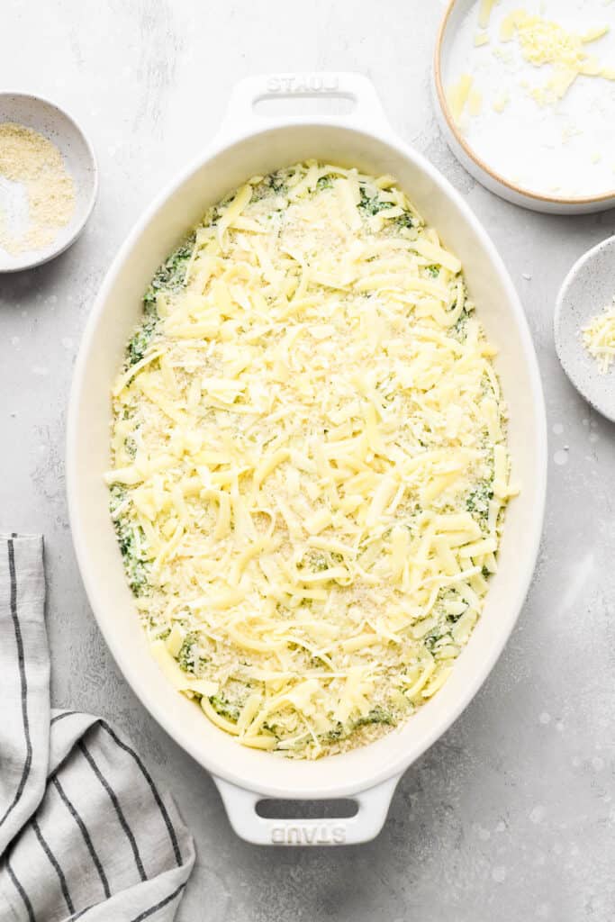 Shredded cheese on top of creamed spinach in a white casserole dish