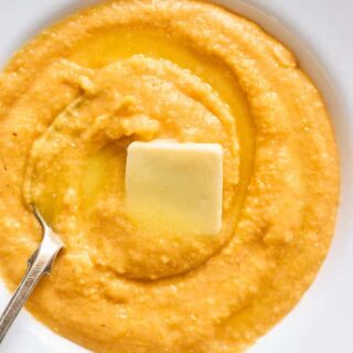 A close up of sweet potato grits in a white bowl with butter melting over the top