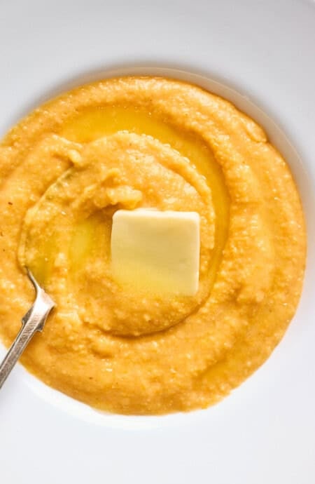 A close up of sweet potato grits in a white bowl with butter melting over the top