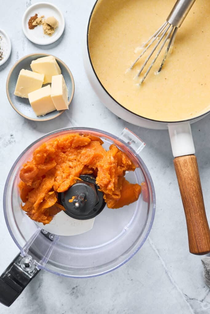 Baked sweet potato flesh in a food processor next to a pot of creamy grits and butter pats