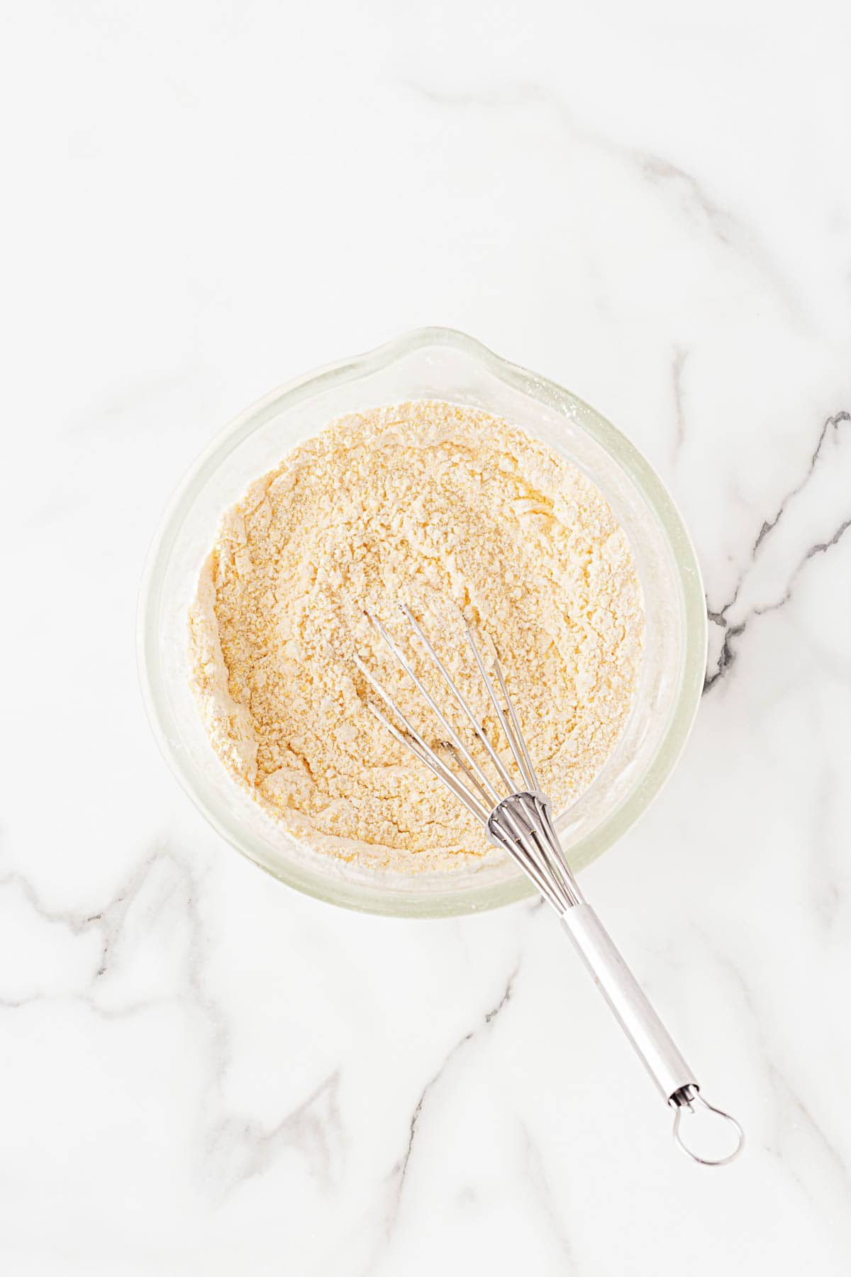 Dry ingredients whisked together in a glass bowl with cornmeal visible