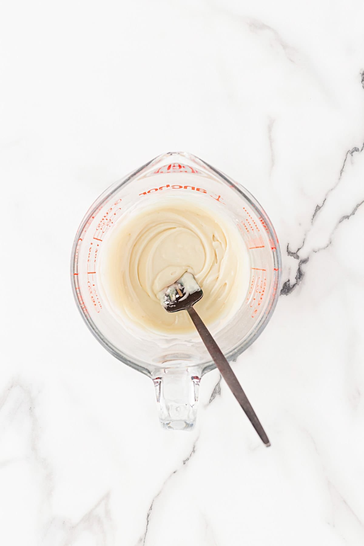 Measuring cup with smooth, creamy lemon glaze and a spoon resting inside