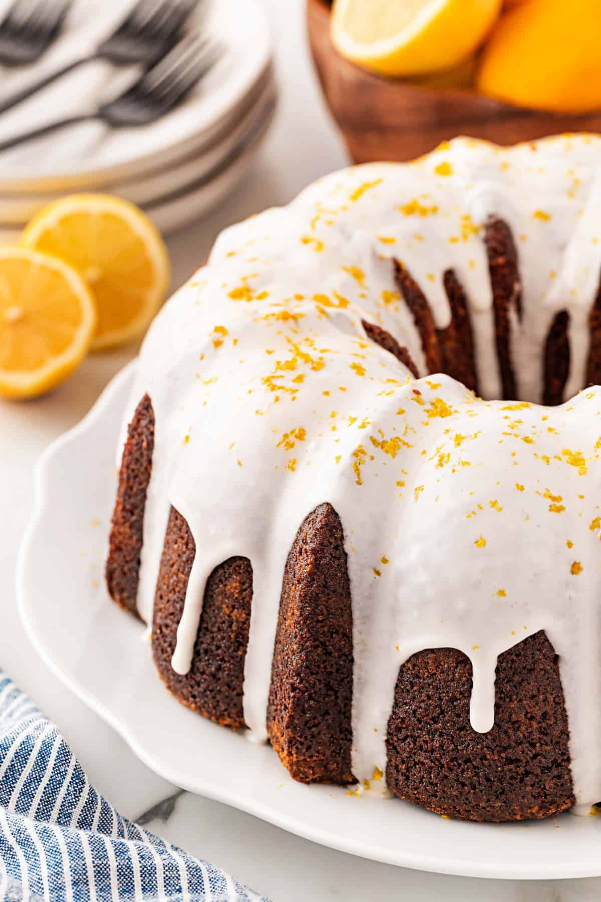 Glazed lemon olive oil Bundt cake on a platter, topped with lemon zest and dripping icing