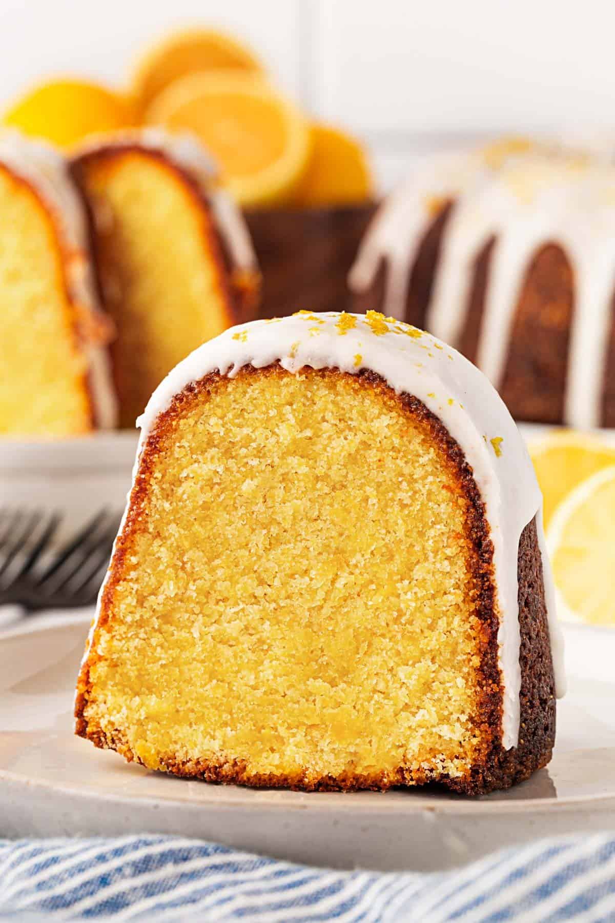 Closeup of a sliced lemon olive oil cake showing the moist, golden crumb with glaze on top and more cake in the background