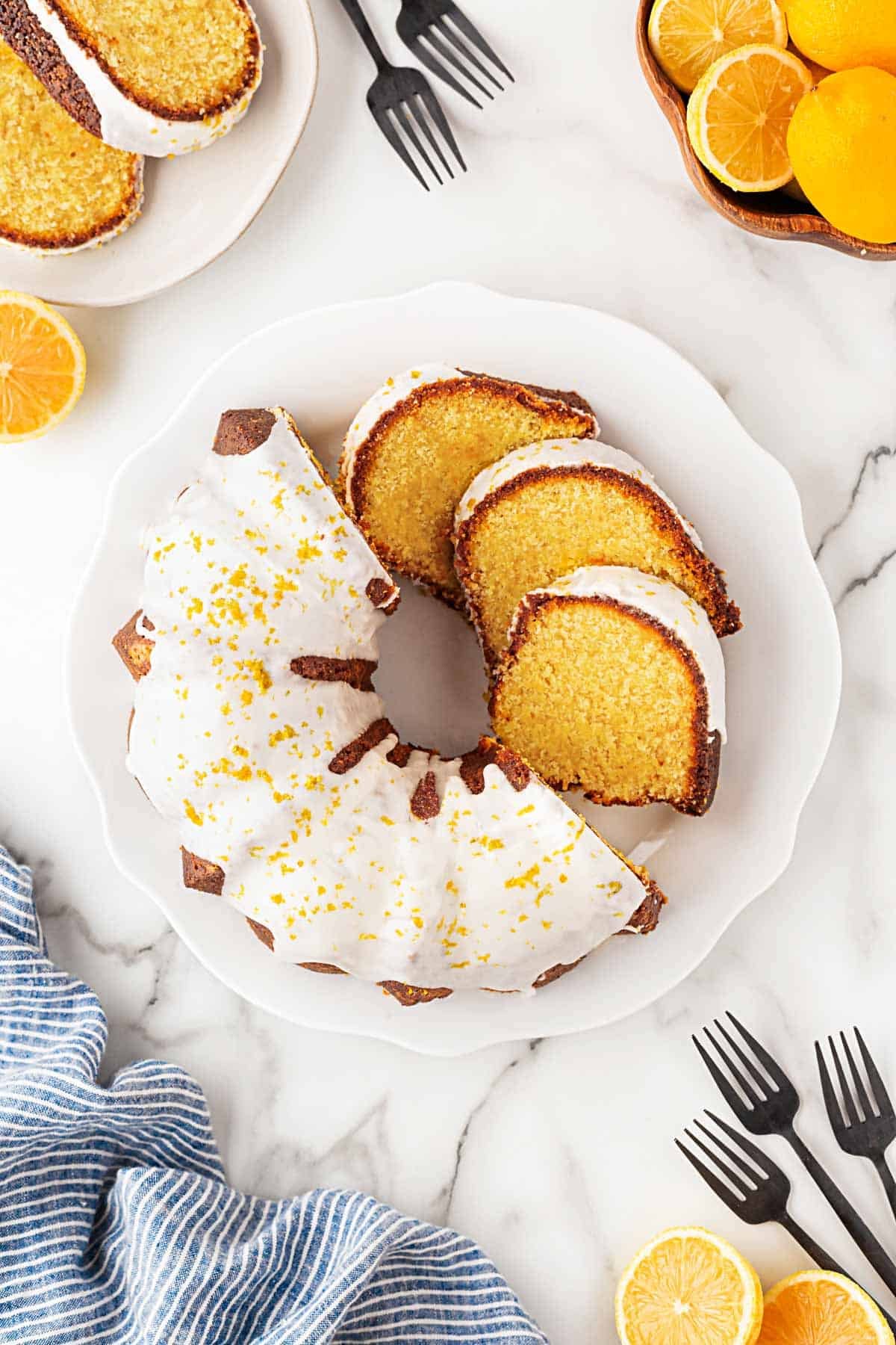 Overhead shot of sliced lemon olive oil bundt cake glazed and garnished with lemon zest on a serving platter