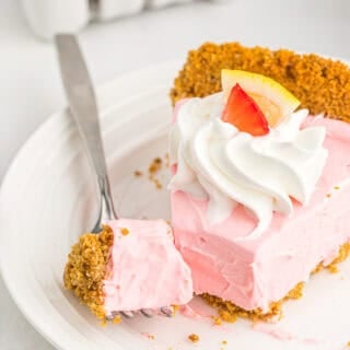 A slice of kool-aid pie on a white plate being cut into with a fork