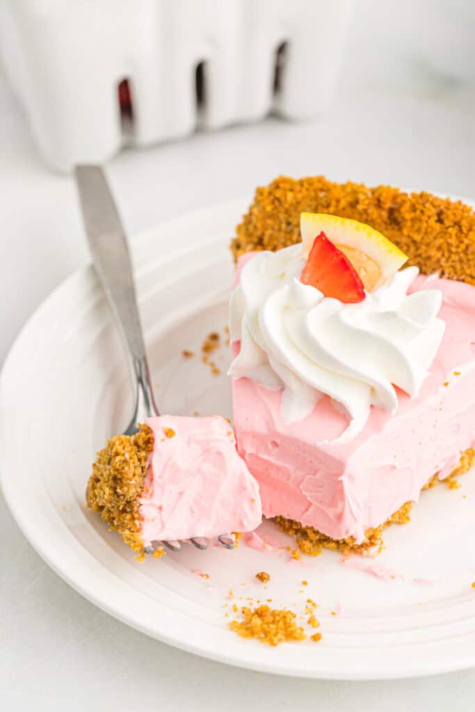 A slice of kool-aid pie on a white plate being cut into with a fork