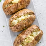 Three baked potatoes on a white tray cut open with butter inside