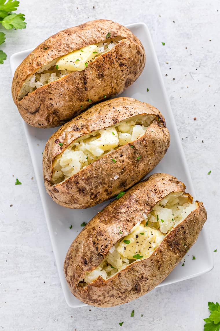 Three baked potatoes on a white tray cut open with butter inside