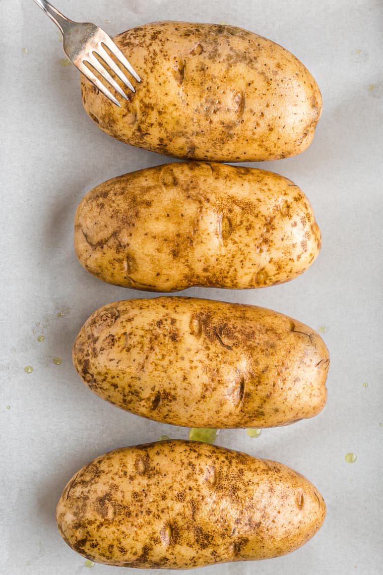 Four russet potatoes being pierced with a fork teaching how to bake a potato