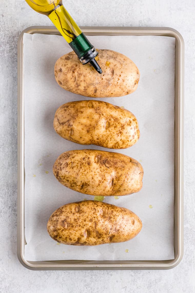 Oil being spread on four russet potatoes on a baking tray showing how to bake a potato