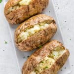 Three baked potatoes on a white tray cut open with butter inside