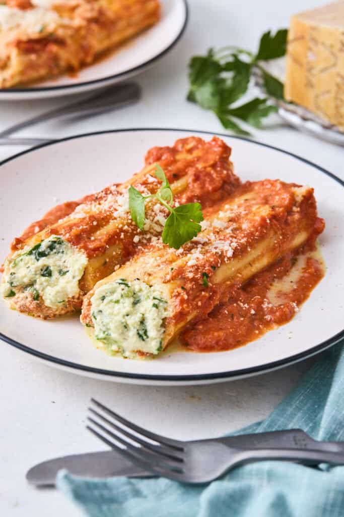 Two stuffed cheese manicotti pasta on a white plate with red sauce spooned on top