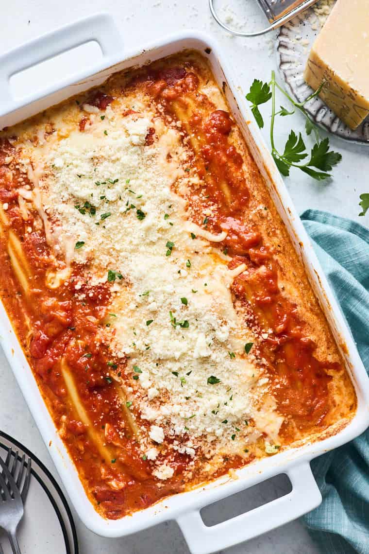 A large baking pan with spinach manicotti stuffed with cheese and topped red sauce and cheese out of the oven