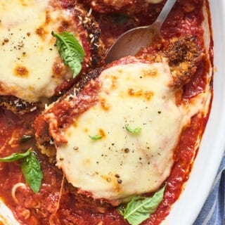 A close up of chicken parmesan being scooped out of white baking pan to serve