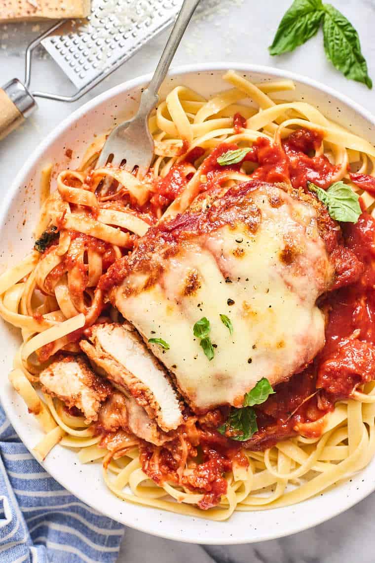 Chicken parmesan on a white plate being served over pasta