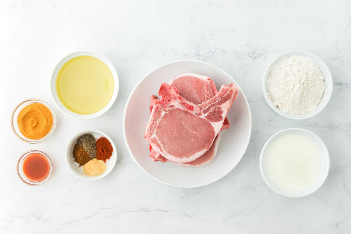 Ingredients to make southern fried pork chops in white bowls on a white background